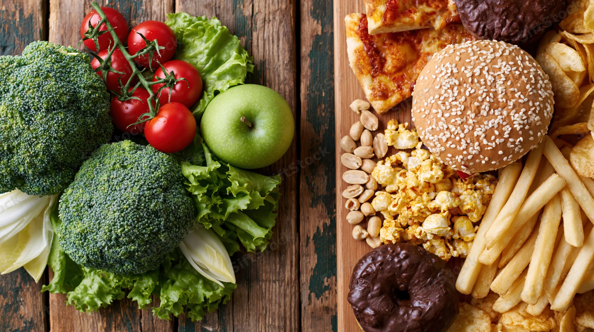 Split flat lay of fresh vegetables and fruits on left versus processed junk food on right on worn wooden table
