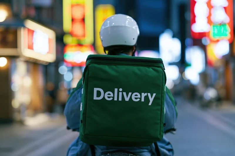 Delivery rider on motorcycle seen from behind in city street at night