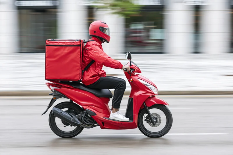 Food delivery rider on red scooter moving through urban street