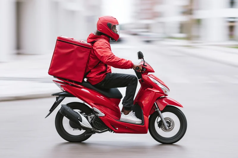 Delivery rider on red scooter moving through urban street