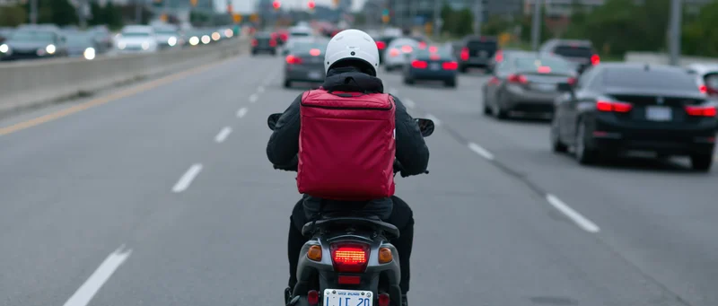 Delivery rider on scooter viewed from behind in heavy traffic on urban highway