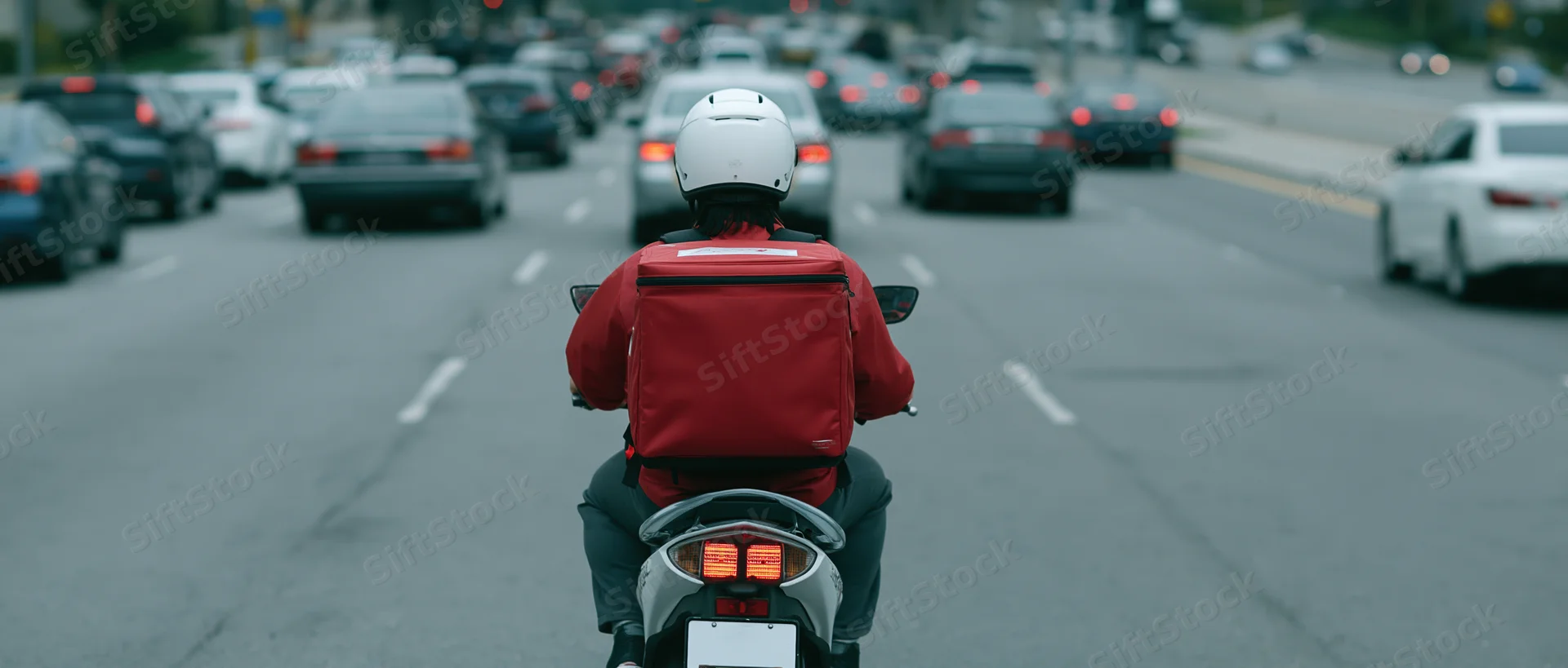 Delivery rider on scooter seen from behind in heavy city traffic