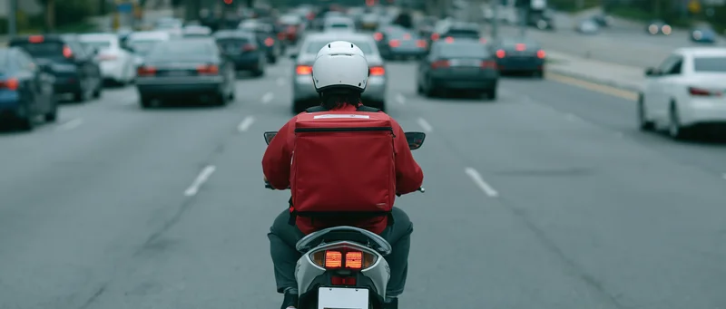 Delivery rider on scooter seen from behind in heavy city traffic