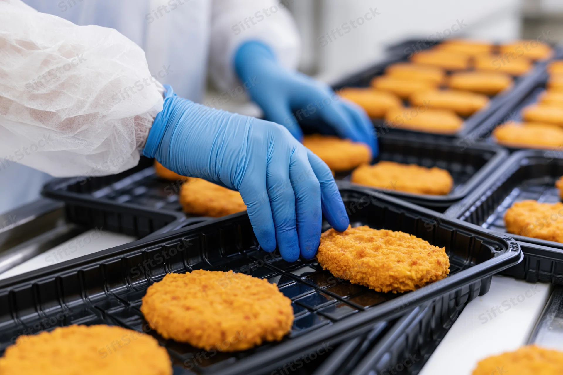Worker placing breaded chicken patties into black plastic trays in a food factory