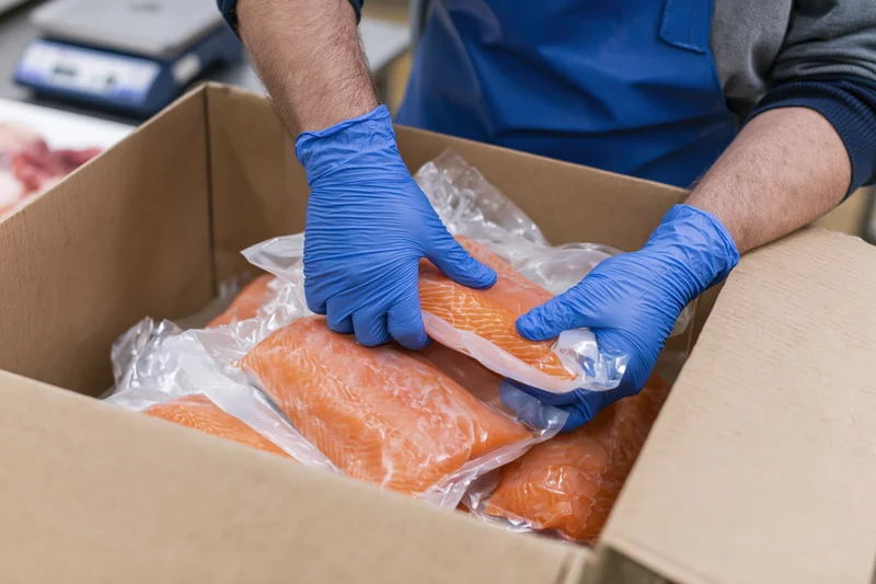 Worker packing vacuum-sealed salmon fillets in a cardboard box