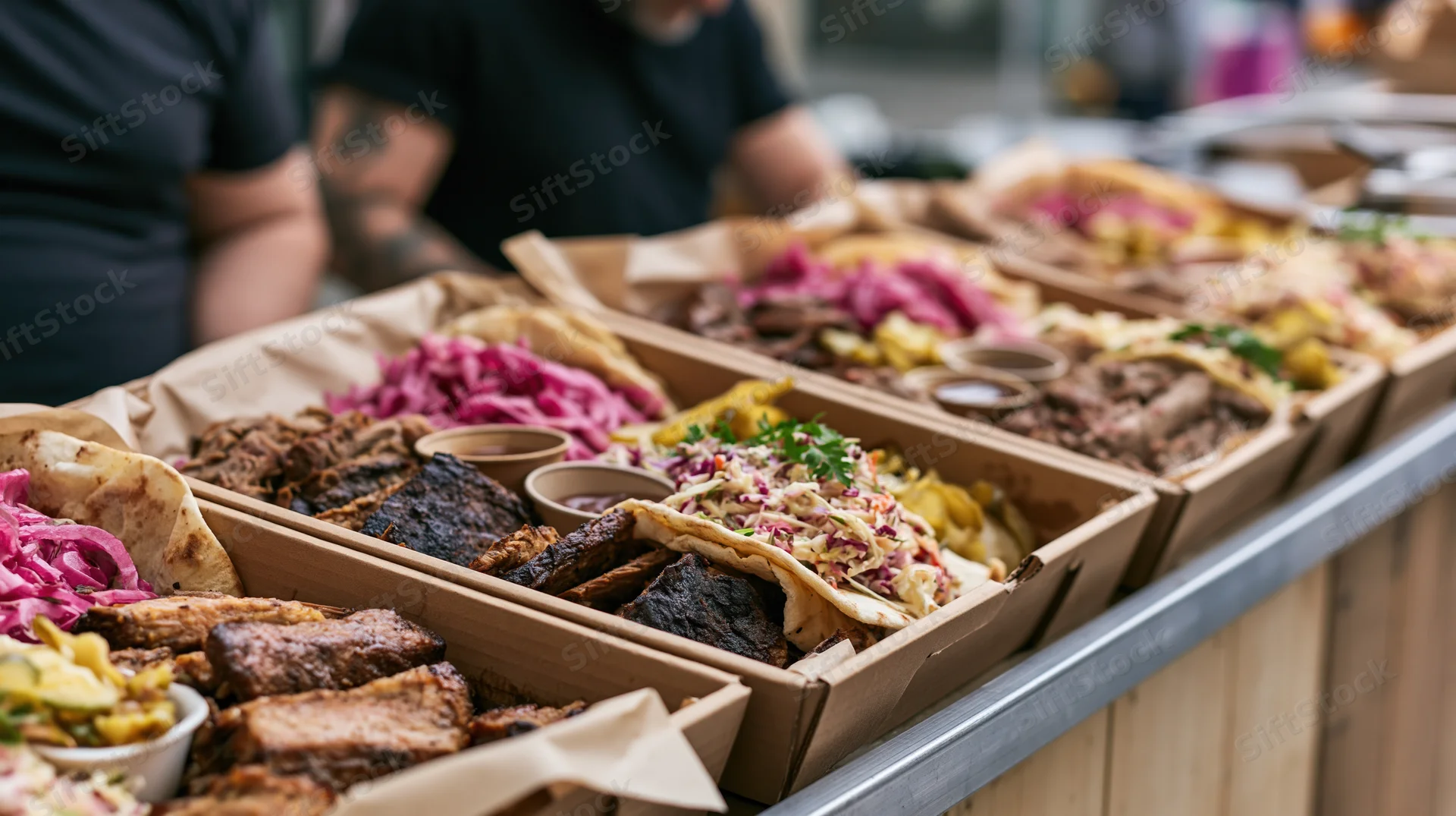 Food stall counter lined with cardboard trays filled with tacos and barbecue meats