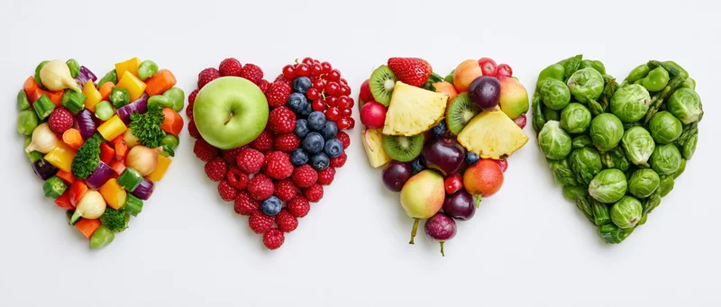 Four heart-shaped arrangements of fruits and vegetables in a row on white background