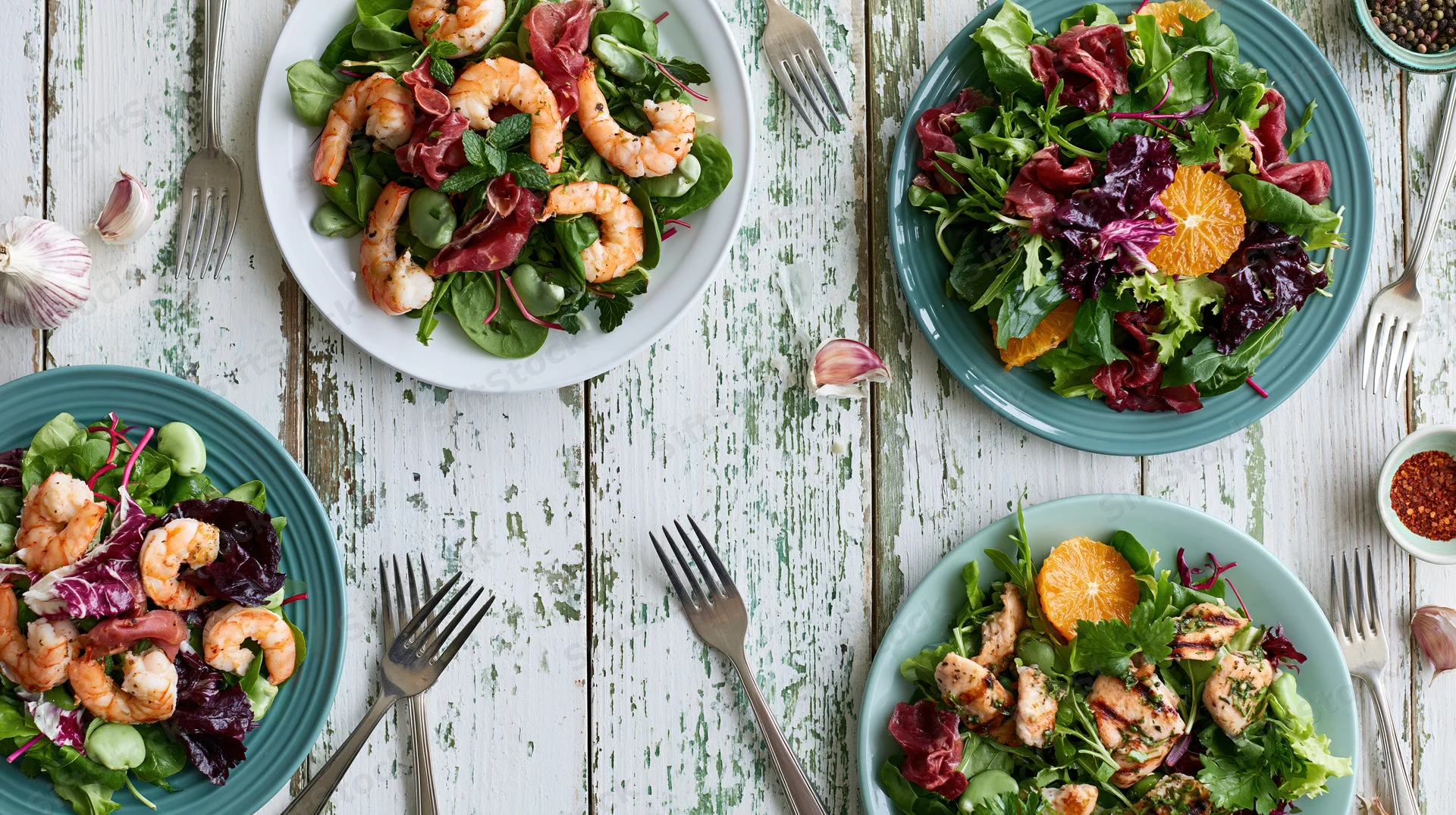 Four salad plates with shrimp and greens arranged overhead on a weathered wooden table
