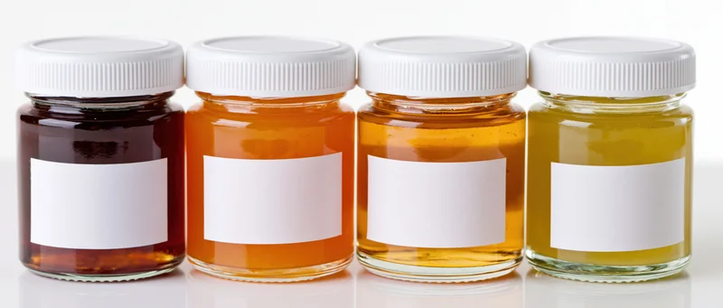 Four glass jars of honey with blank white labels lined up on a white surface