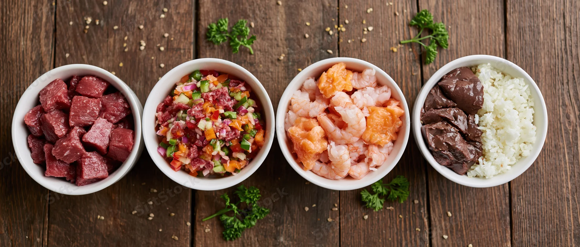 Four white bowls with beef, shrimp, salmon, and chocolate rice arranged in a row on a wooden table