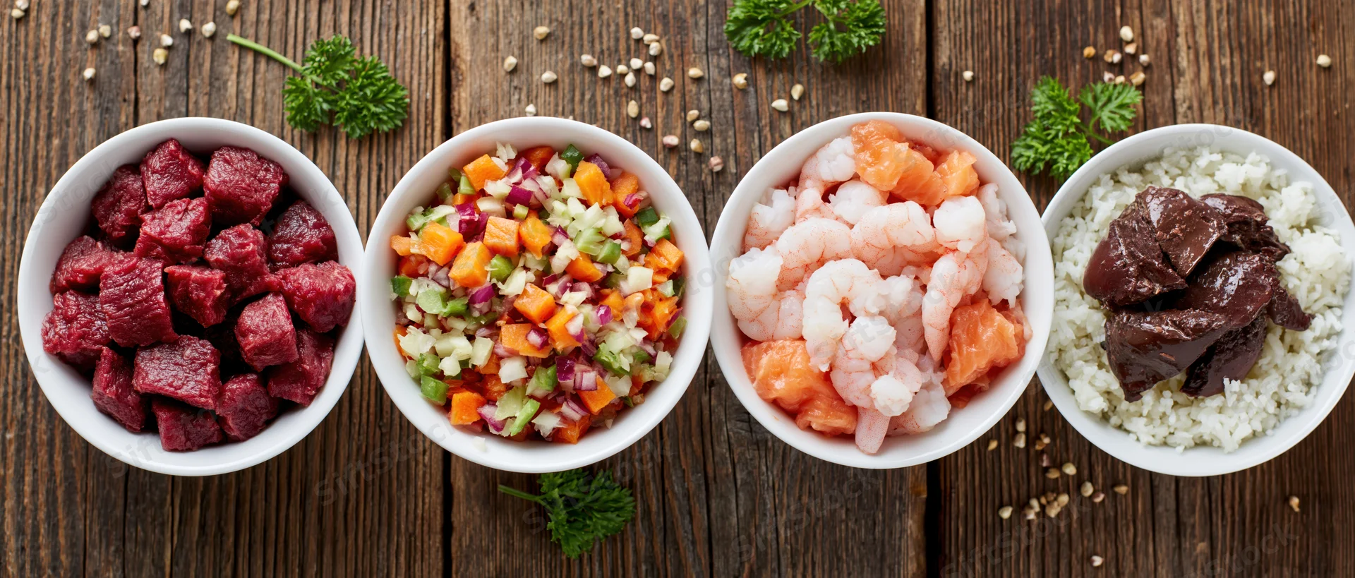 Four white bowls with different protein and vegetable dishes arranged in a row on a wooden table