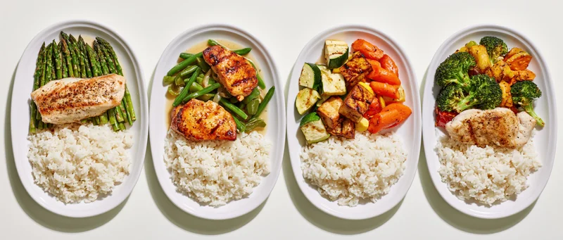 Four white ceramic plates arranged side by side in a flat lay, each with rice, protein and vegetables