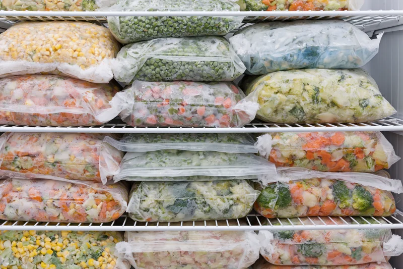 Freezer shelves packed with clear plastic bags of frozen vegetables arranged in rows