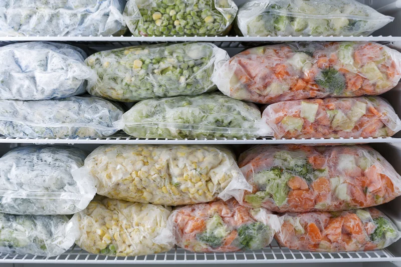 Frozen vegetables in clear plastic bags arranged on freezer shelves