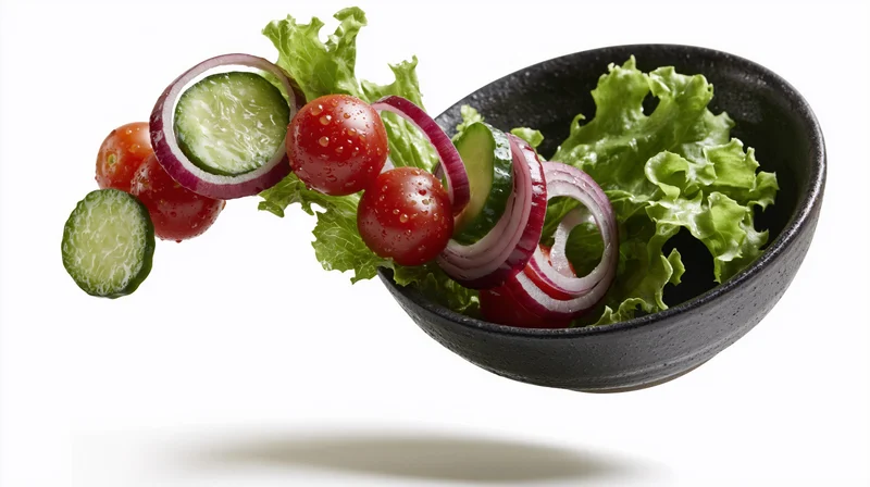 Fresh salad ingredients falling into a dark ceramic bowl against white background