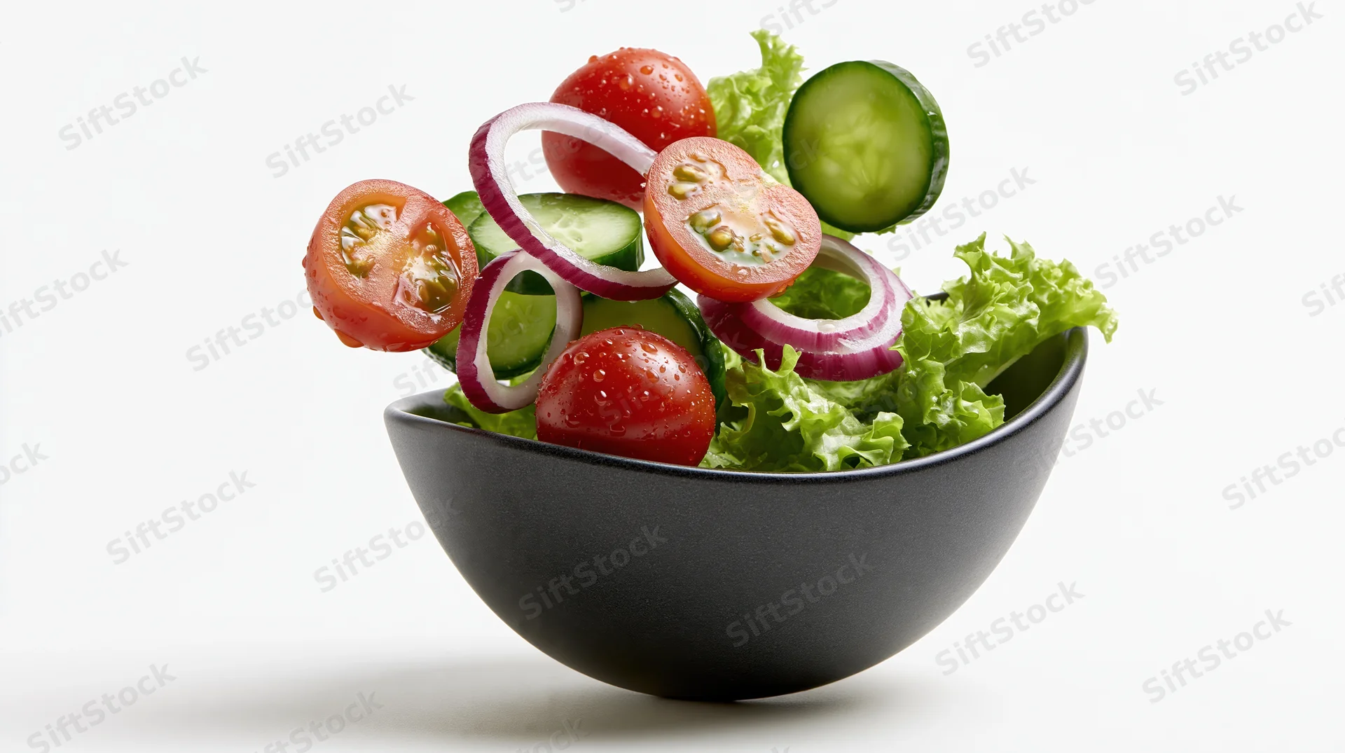 Fresh garden salad ingredients floating above a dark ceramic bowl on white background