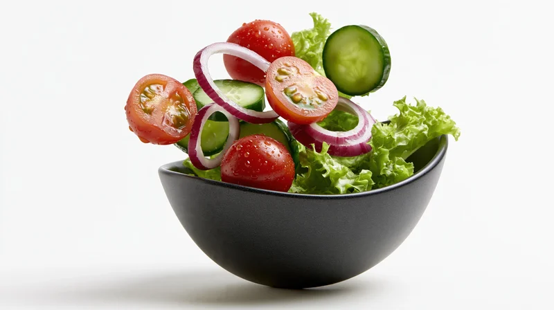 Fresh garden salad ingredients floating above a dark ceramic bowl on white background