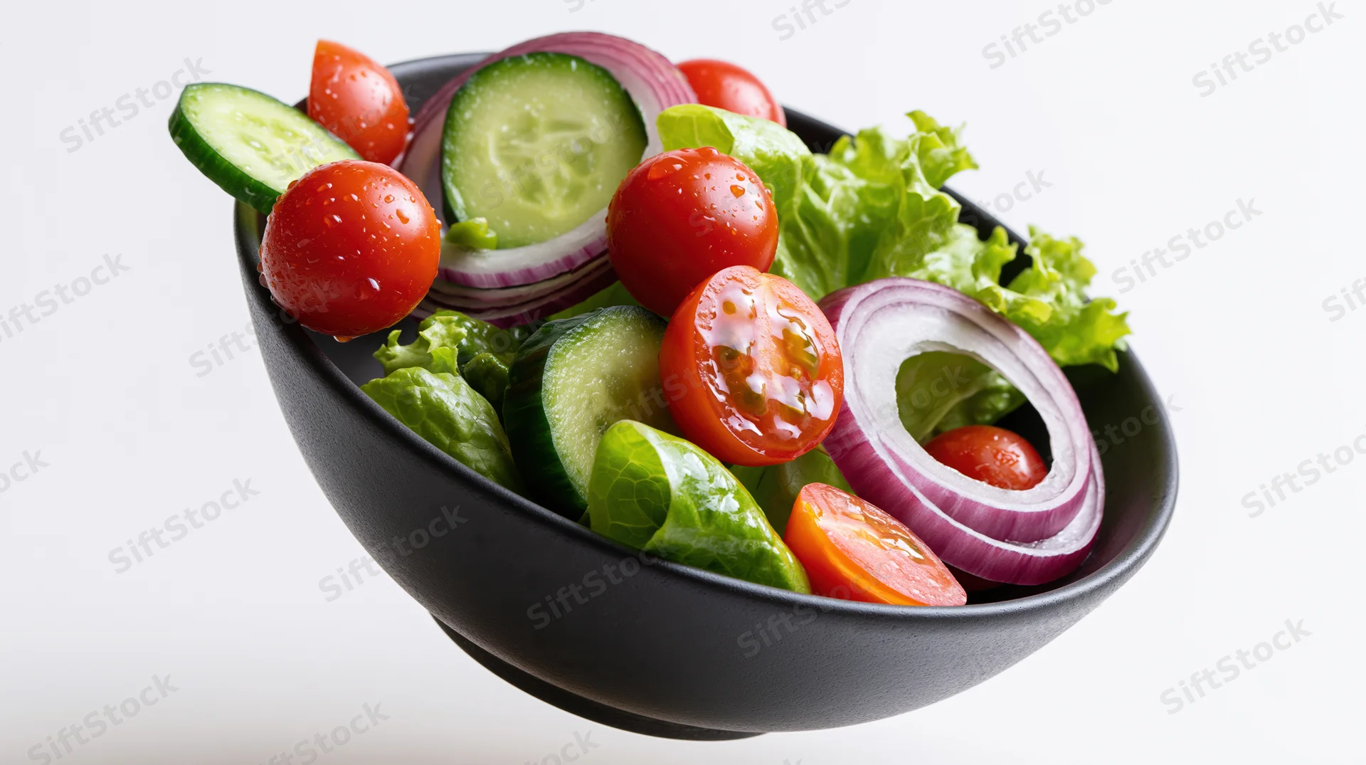 Fresh garden salad ingredients in a dark ceramic bowl with water droplets on a white background