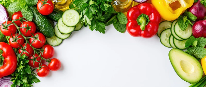 Fresh salad ingredients arranged as a border frame along the top and sides of a white surface with copyspace in the center