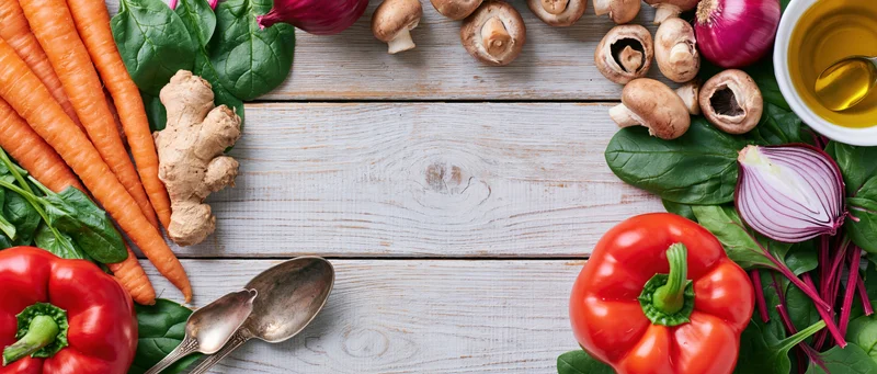 Fresh vegetables and cooking utensils arranged in a flat lay on a wooden table