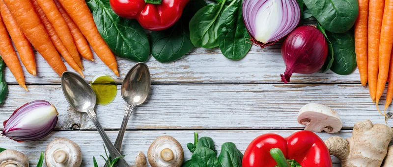 Fresh vegetables and cooking utensils arranged in a flat lay on a white wooden table