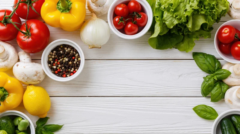 Fresh vegetables and herbs arranged in a border frame around a white wooden table with copyspace in center
