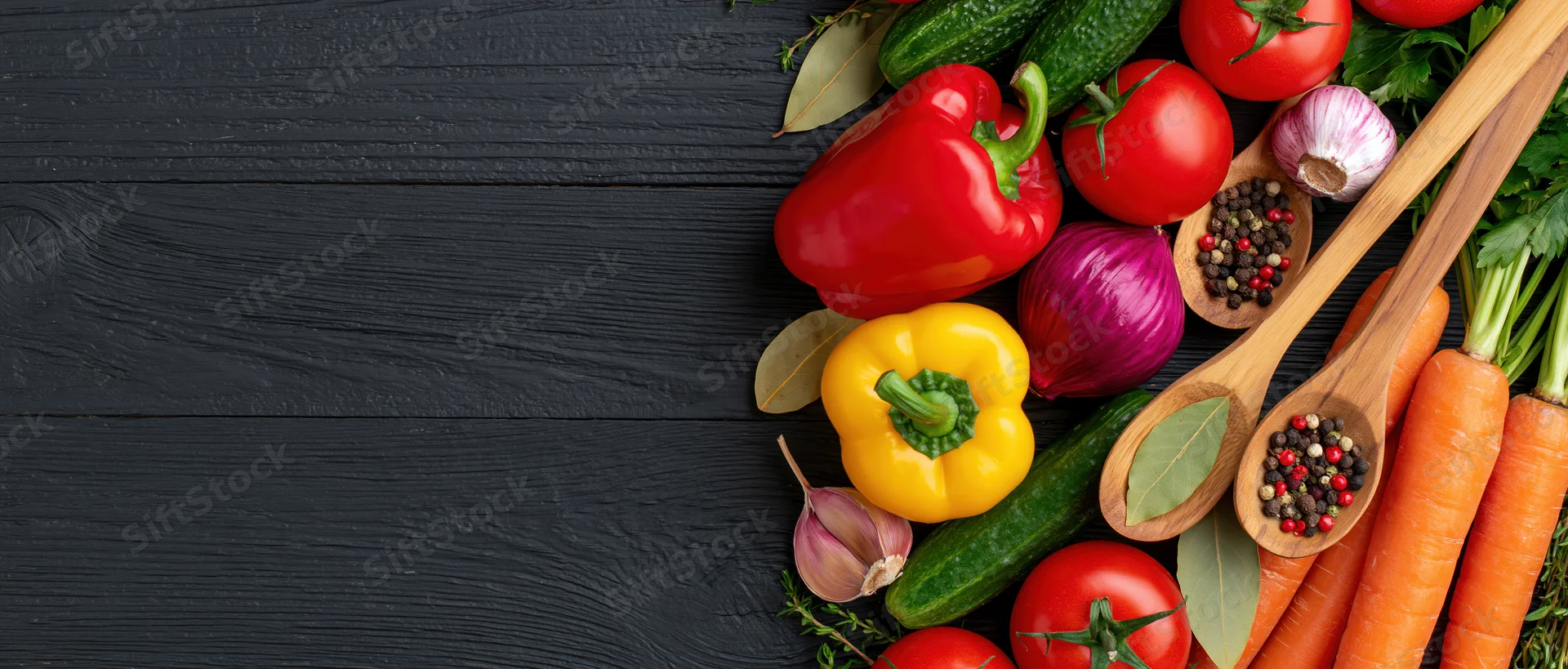 Fresh vegetables and spices arranged along the right edge of a black wooden surface with copyspace on the left