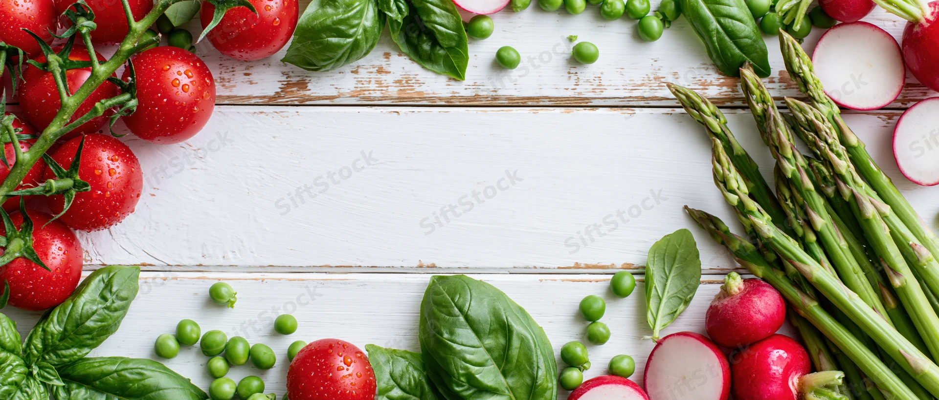 Fresh vegetables arranged along the edges of a white wooden table with copyspace in the center