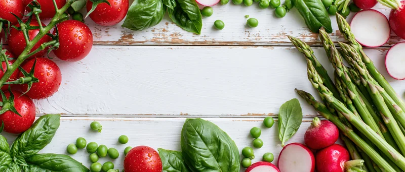 Fresh vegetables arranged along the edges of a white wooden table with copyspace in the center