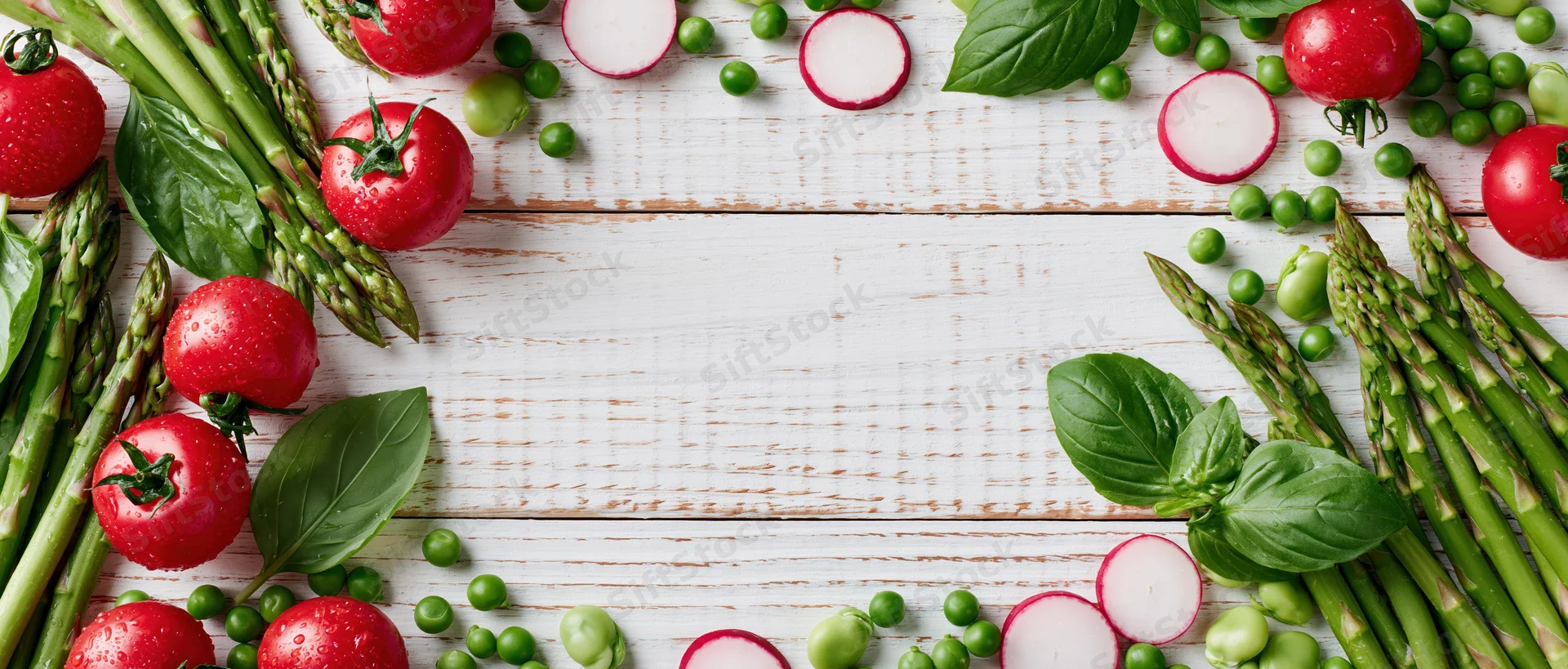 Fresh vegetables arranged along the edges of a white wooden table with copyspace in center