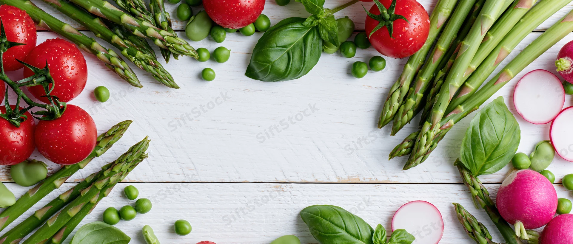 Fresh vegetables arranged along edges of white wooden table with central copyspace