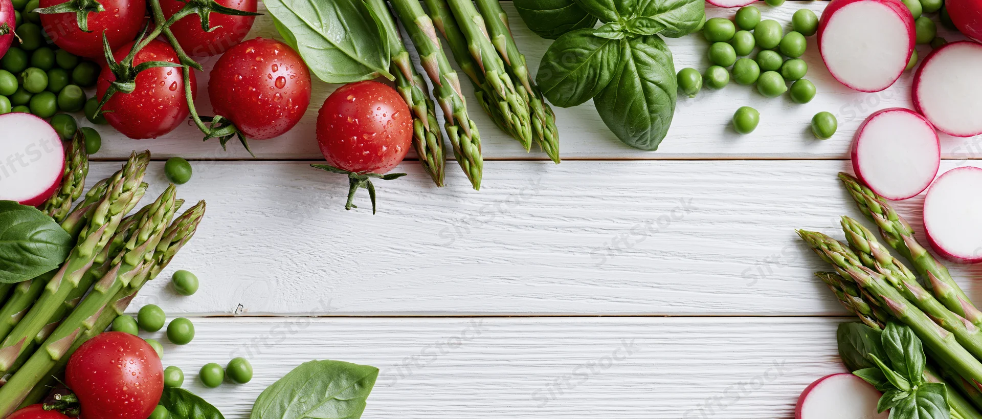 Fresh vegetables arranged along edges of white wooden table with central copyspace