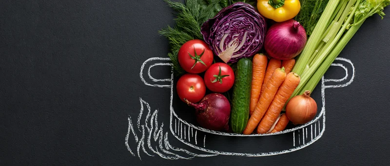Fresh vegetables arranged in a chalk-drawn pot on a black surface with copyspace on the left