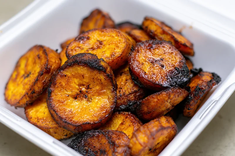 Fried sweet plantain slices piled in a white styrofoam container