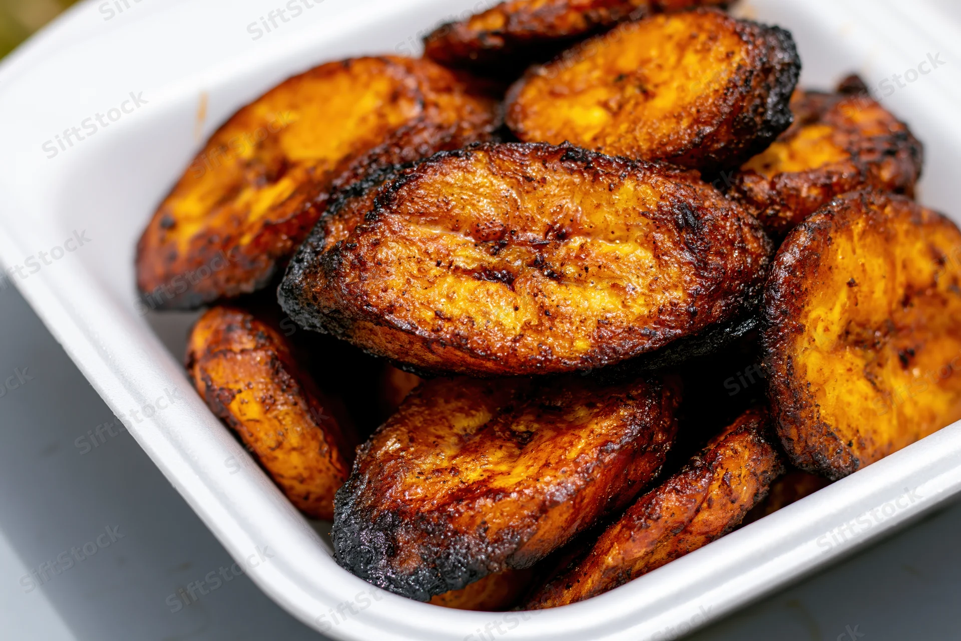 Fried sweet plantain slices piled in a white styrofoam container