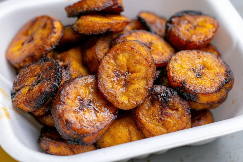 Fried sweet plantain slices piled loosely in a white styrofoam container