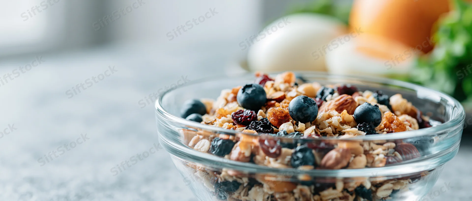 Glass bowl filled with granola, blueberries, nuts and dried fruit on a kitchen countertop