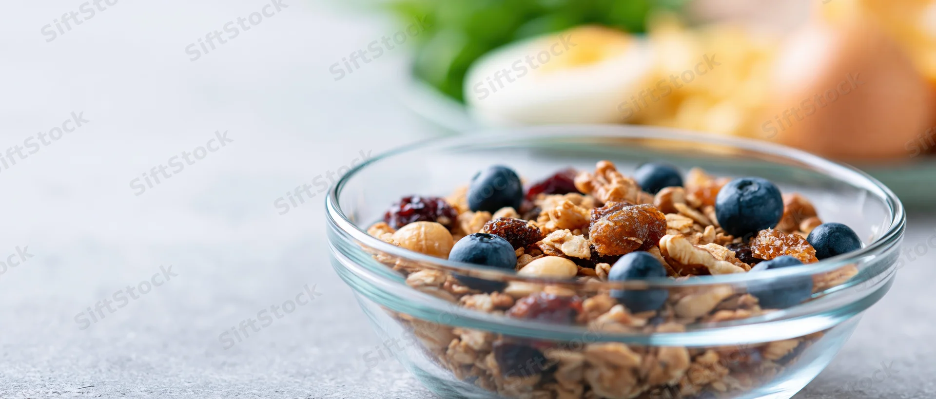 Glass bowl filled with granola, blueberries, dried fruit and nuts on a kitchen countertop