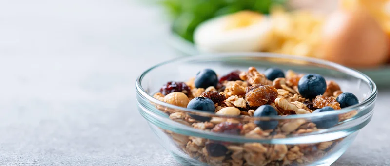 Glass bowl filled with granola, blueberries, dried fruit and nuts on a kitchen countertop