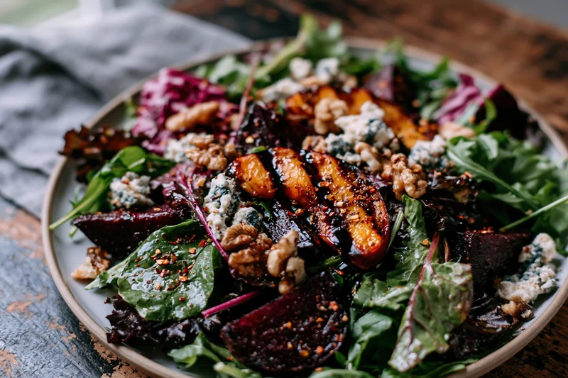 Grilled peach and roasted beet salad on a plate with greens, blue cheese and walnuts on a wooden table