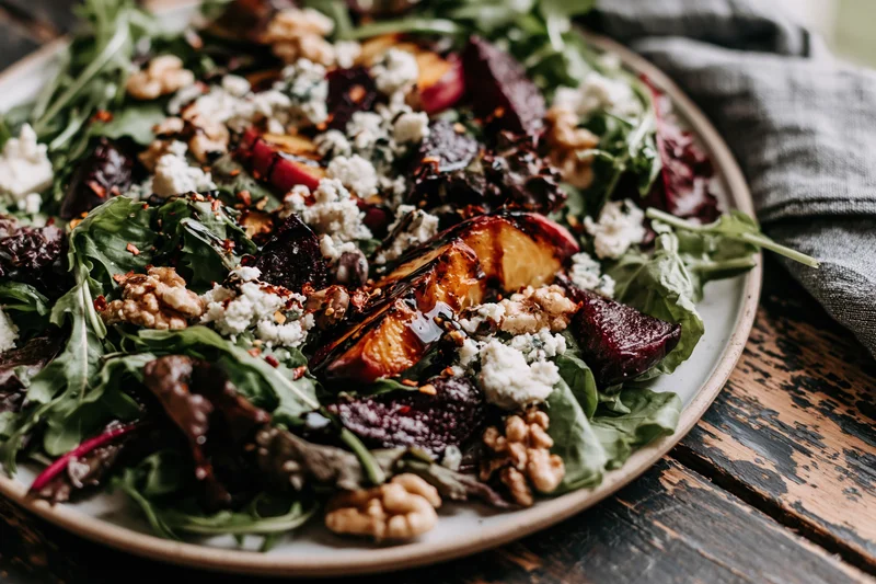 Grilled peach and roasted beet salad with arugula, feta, and walnuts on a rustic wooden table