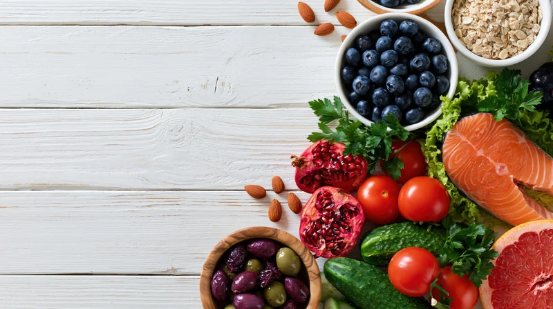 Healthy food flat lay arranged along right edge of white wooden table with copyspace on left