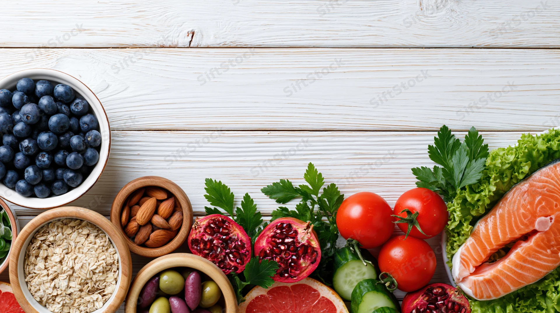 Healthy food flat lay arranged along the right edge of a white wooden table with copyspace on top