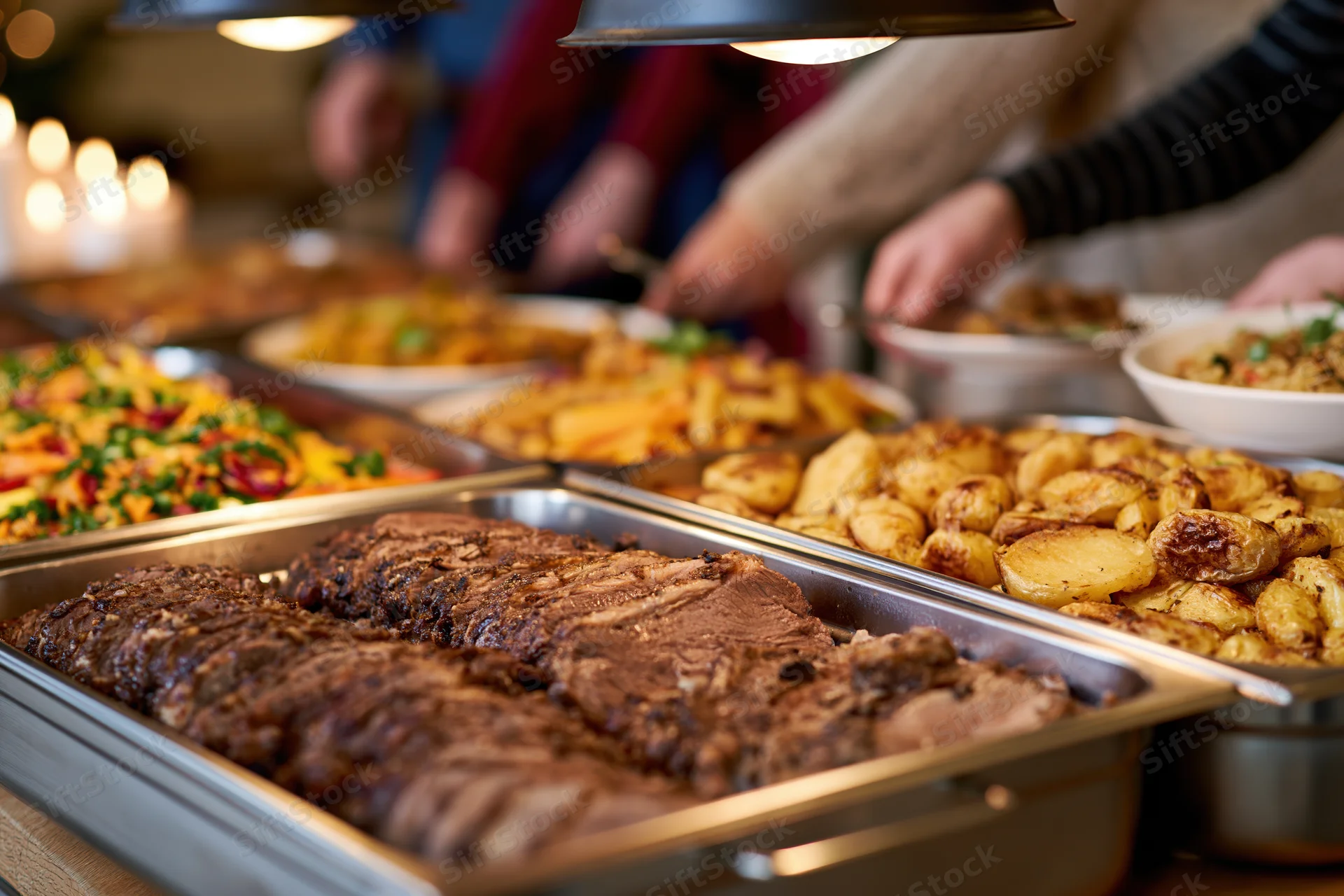 Holiday buffet with sliced roast meat and roasted potatoes served on stainless trays under warm lights