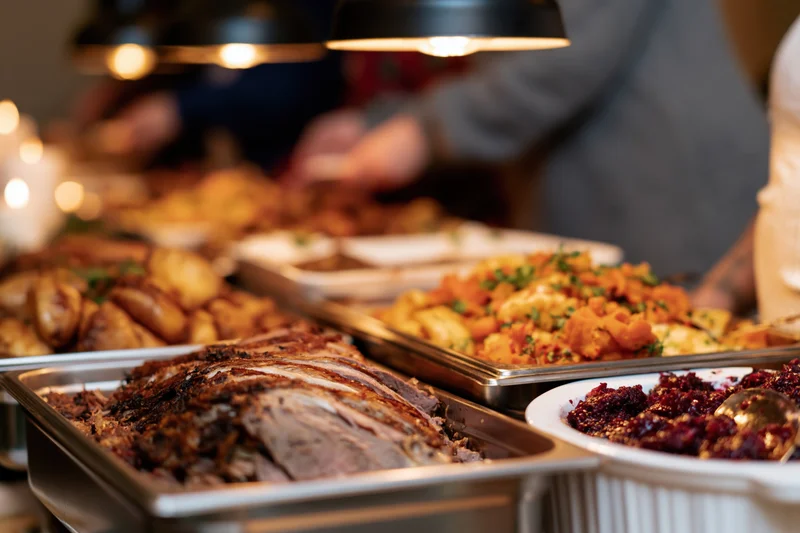 Sliced roast meat and roasted potatoes on a buffet table under heat lamps during a holiday dinner gathering