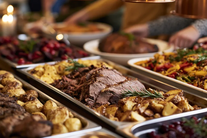 Holiday buffet spread with sliced roast meat and roasted potatoes on metal trays, set for a dinner party