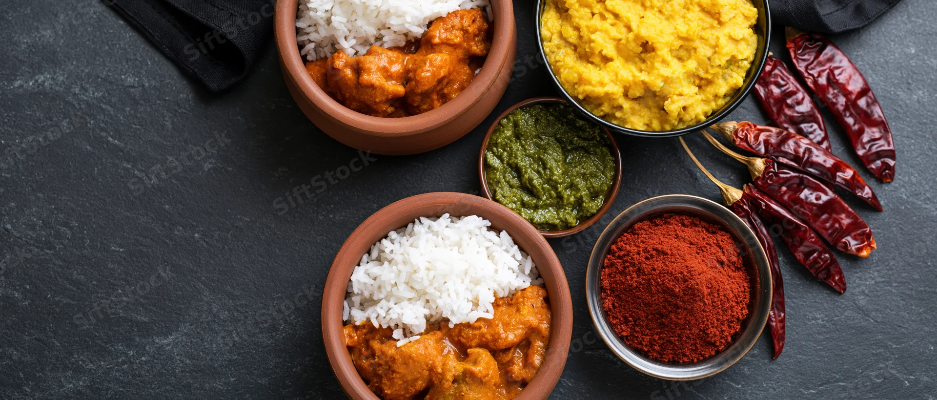 Indian meal with curry and rice in clay bowls arranged on dark slate surface overhead