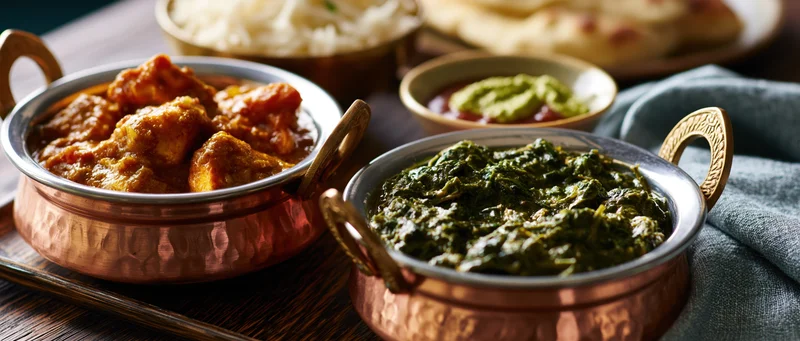 Indian curry and palak paneer served in copper bowls on a dark wooden table with rice and naan bread