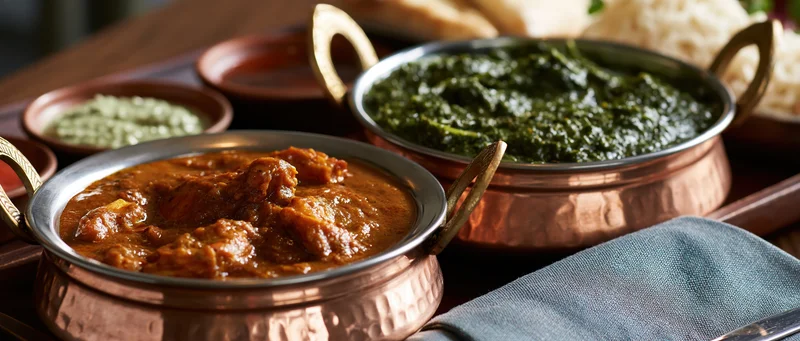 Indian meal with mutton curry and palak saag served in copper bowls on dark wooden table