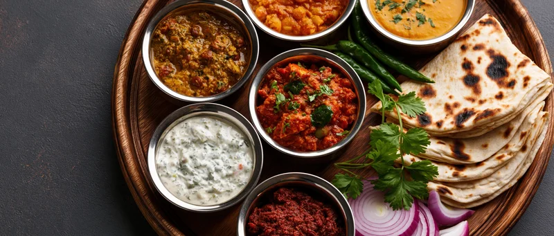 Indian thali meal with multiple curries and roti served on a round wooden tray